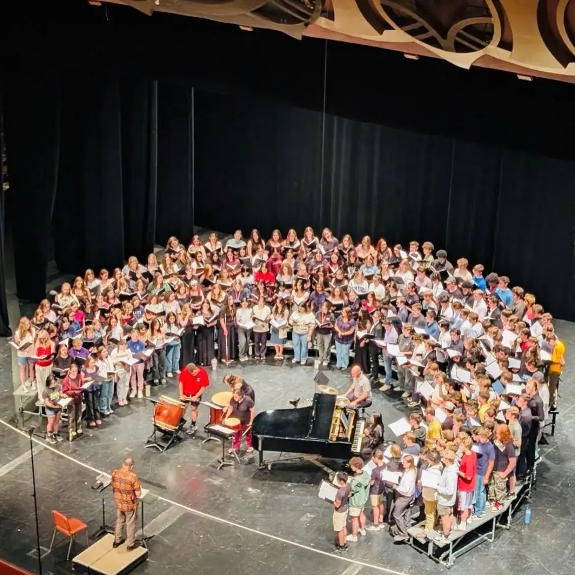 The 2026 All-State Choir seen from above, hundreds of singers around a grand piano