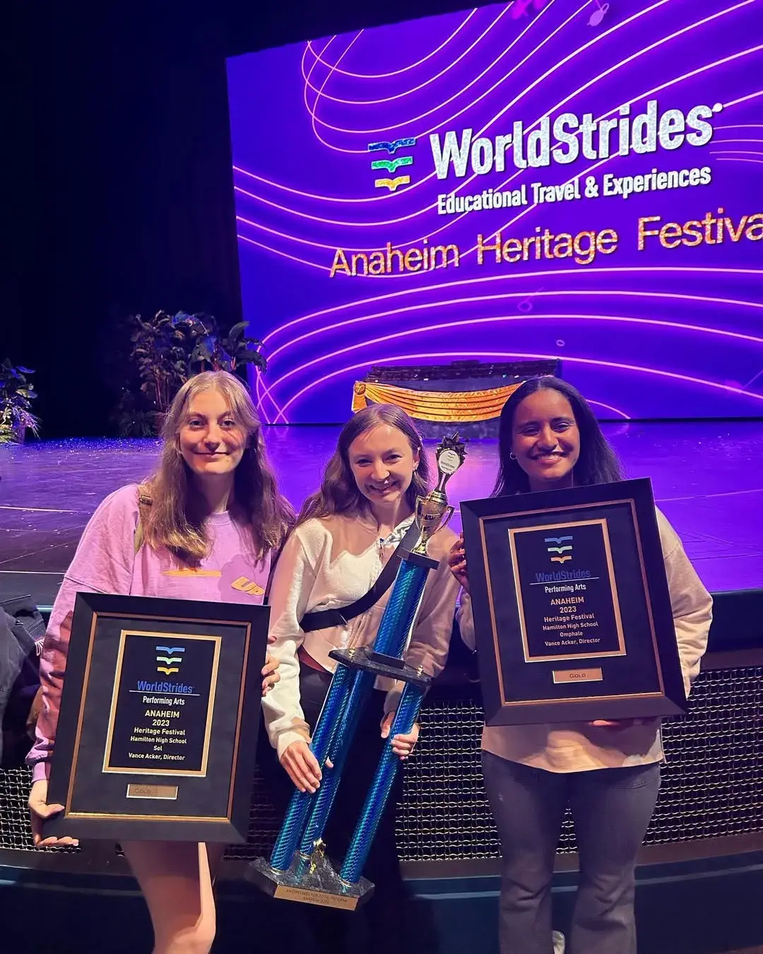 Three Hamilton singers on stage in Anaheim holding festival award plaques and the sweepstakes trophy