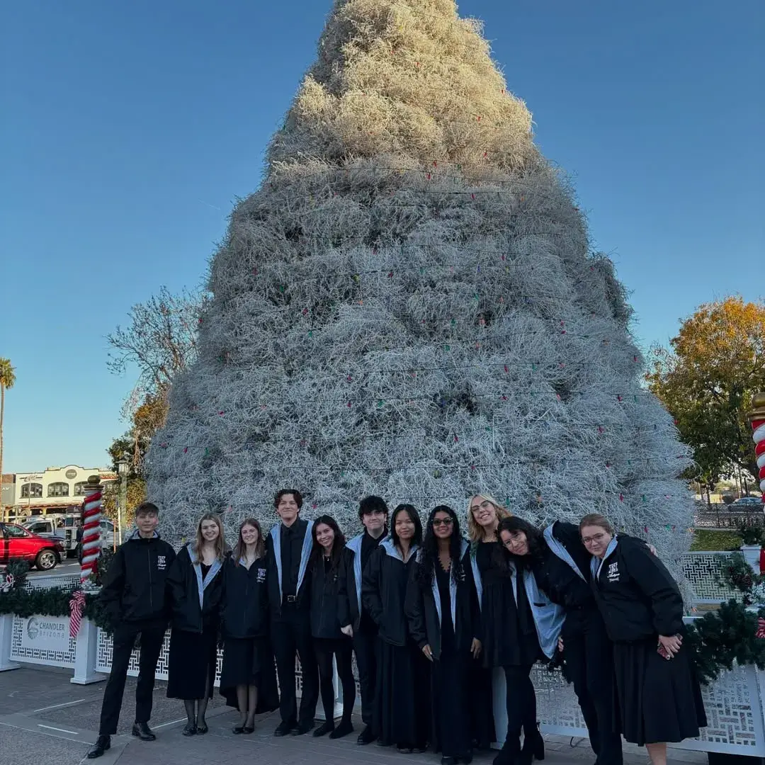 Singers in winter coats in front of a tall white holiday tree