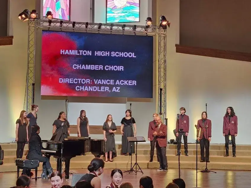 AntiquaNova chamber choir singing around a grand piano on stage