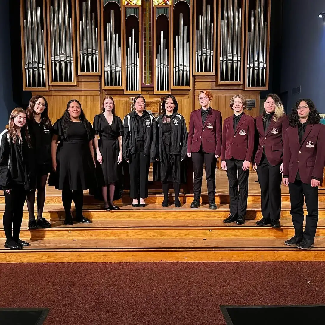 Hamilton singers in maroon and black lined up in front of a pipe organ