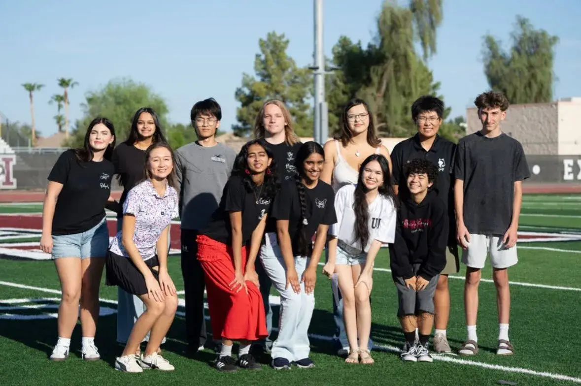 A group of smiling Hamilton singers on the football field after singing the national anthem