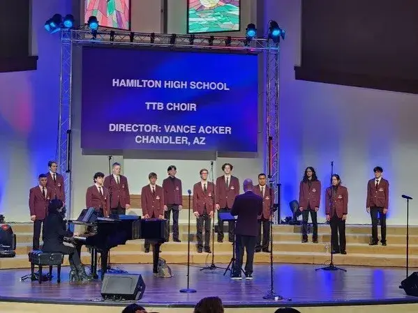 Orpheus in maroon jackets performing on stage in Anaheim under a screen reading Hamilton High School TTB Choir